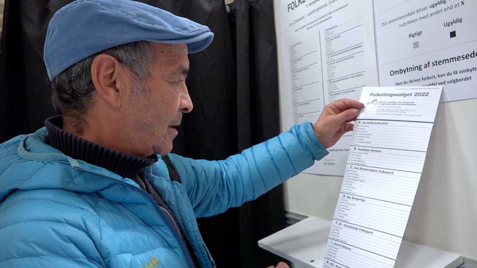 En mand, der står i en stemmeboks, kigger på stemmesedlen til et folketingsvalg